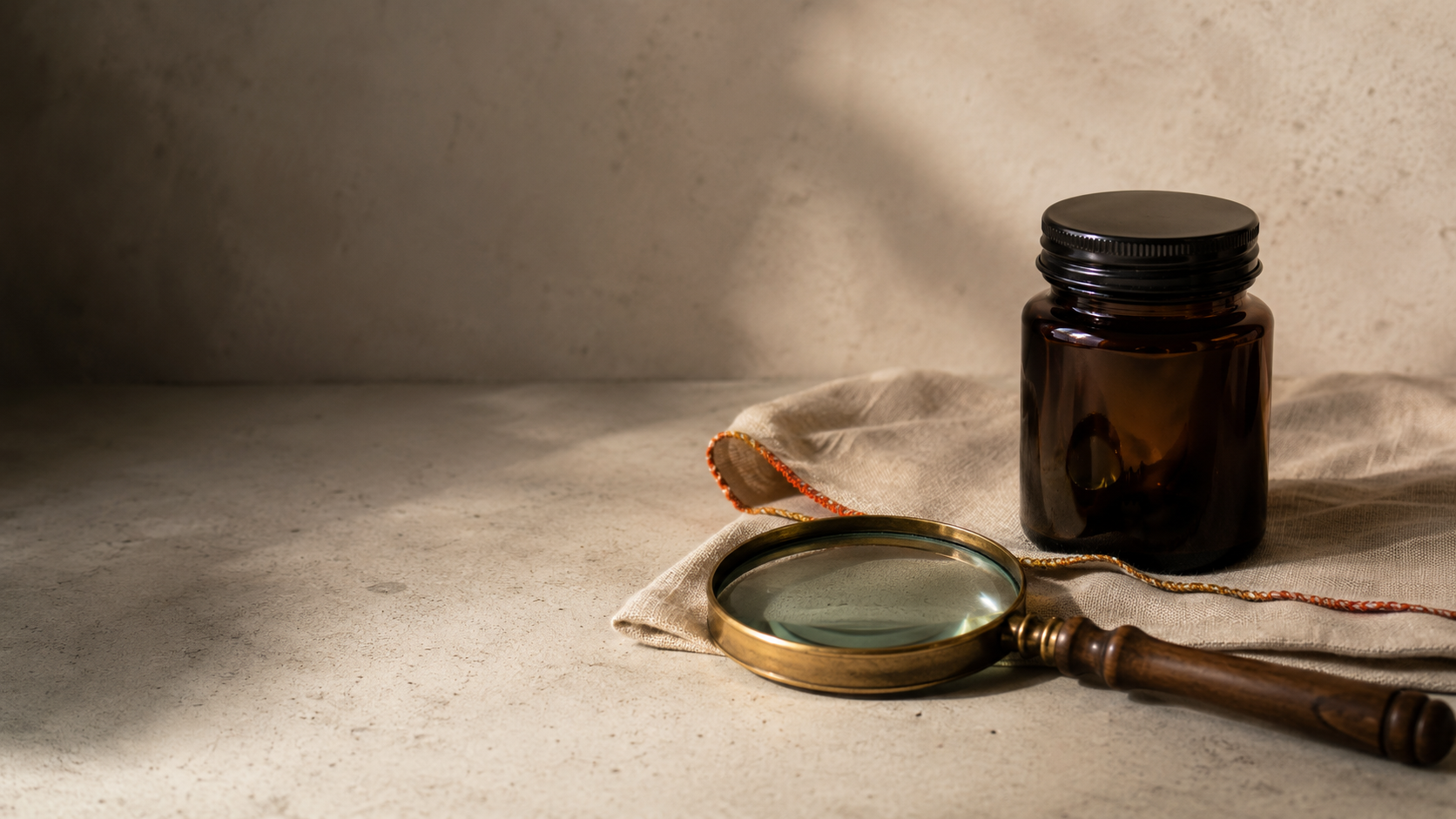 Unbranded amber glass jar beside a vintage magnifying glass on a neutral stone surface, symbolizing careful examination of the synthetic cannabinoid CB9 in a calm editorial setting.