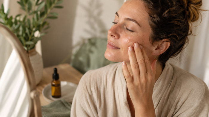 Frau trägt sanft CBD-Serum auf ihre Wange auf und pflegt ihre Haut in einer ruhigen, natürlich beleuchteten Wellness-Umgebung.