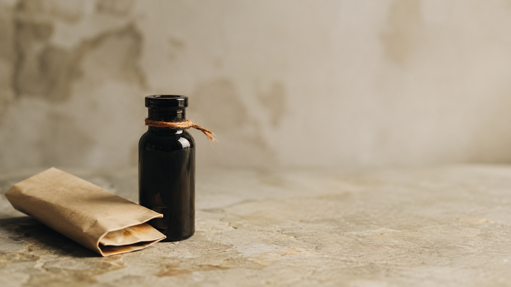 Unmarked dark glass vial with loosely draped natural twine beside folded kraft paper on a muted stone surface, symbolizing the careful examination of synthetic cannabinoids and their risks.